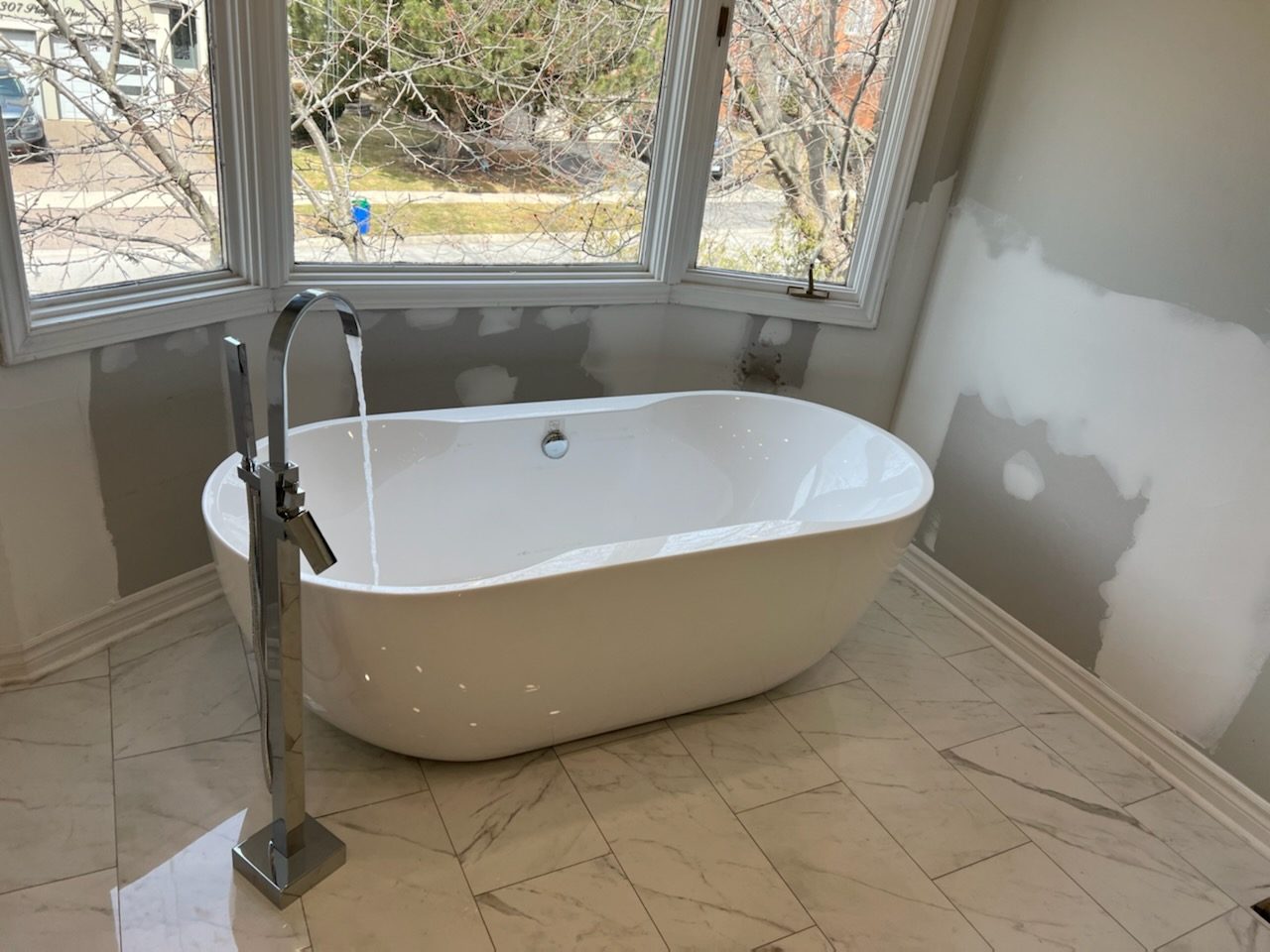 Freestanding bathtub with marble-look floor tile beneath a bay window